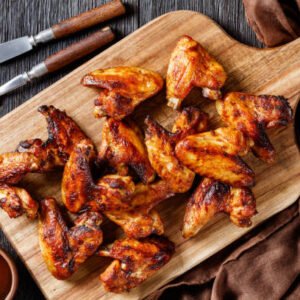 crispy fried chicken wings served on a wooden board with barbeque sauce on dark wooden table, flat lay